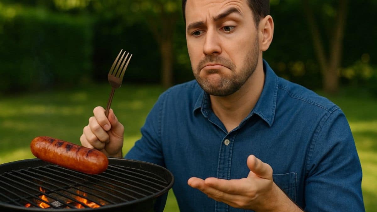 Un homme hésite à piquer une saucisse posée sur un barbecue avec une fourchette.