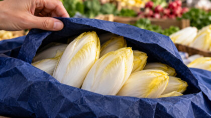 Une main soulève le papier bleu entourant des endives sur un étal